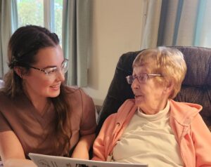 Kendal at Ithaca caregiver, Kieren H. reads with resident Ann B.